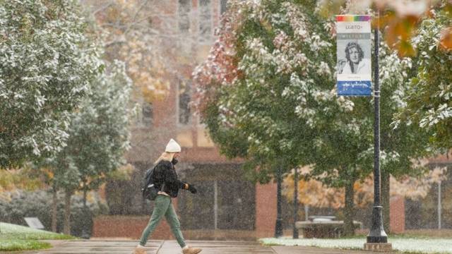 College students walking past building while snow is falling.