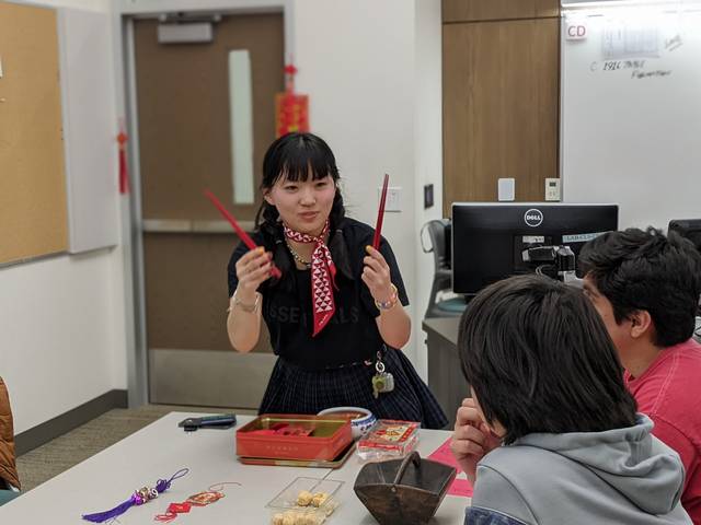 A woman talking to a group while holding chopsticks