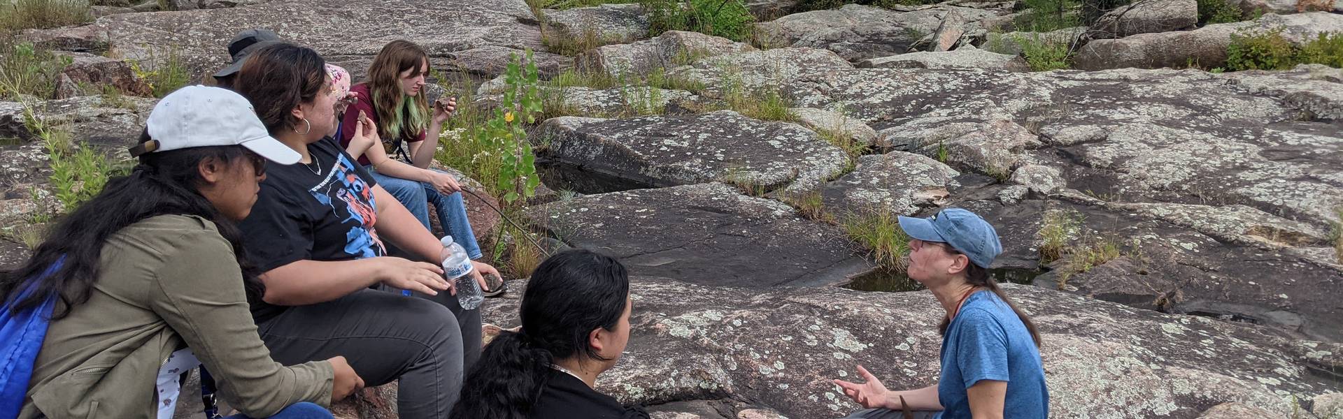 A group gathers on a formation of rocks listening to an instructor