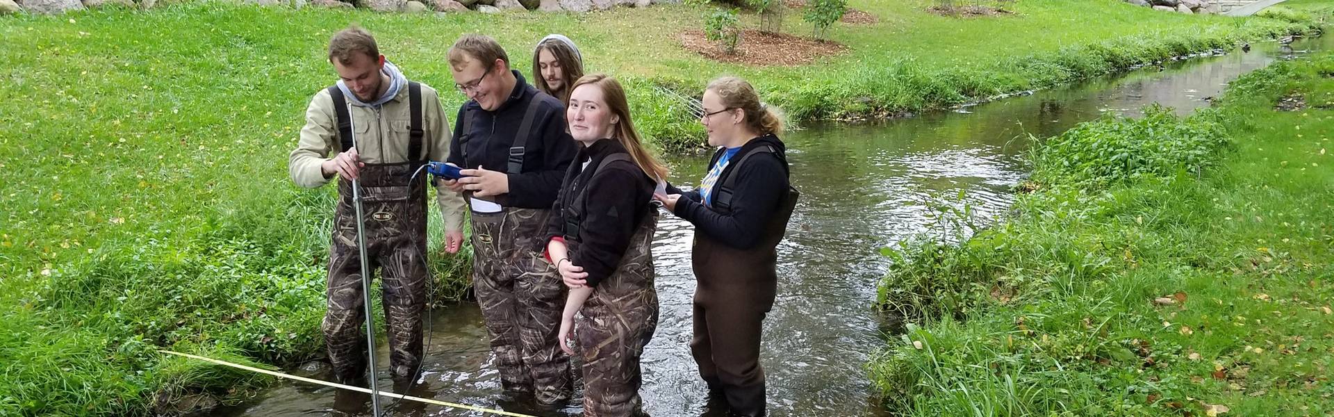 Students collecting water samples in a stream on campus