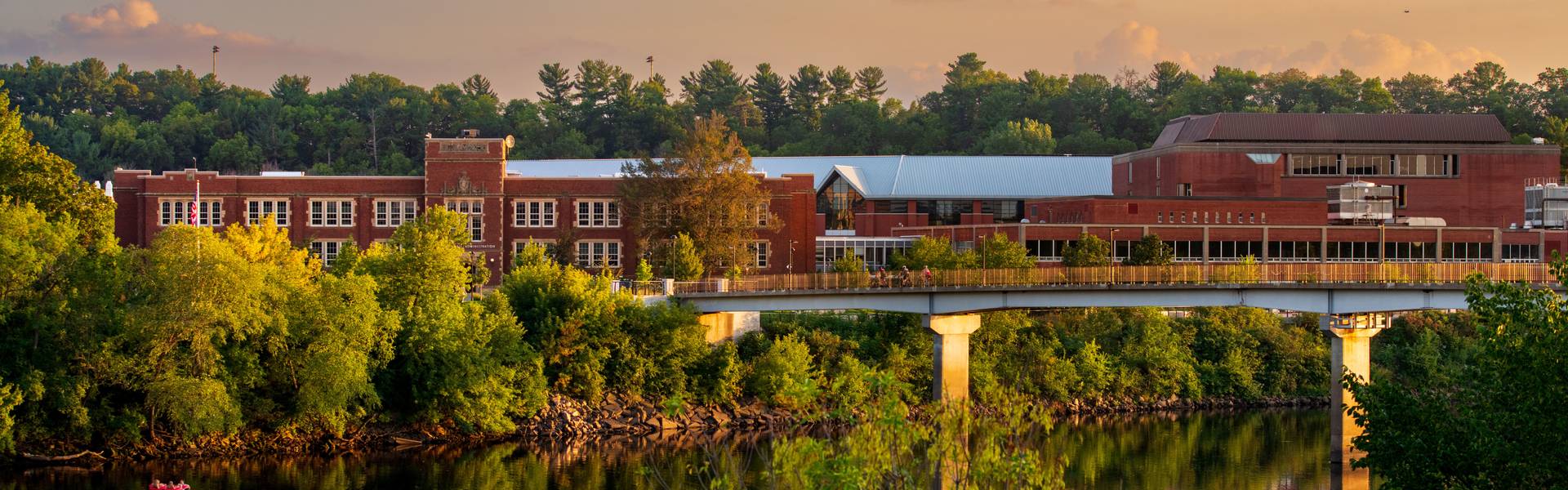 A view of Schofield Hall, a brick building, across the river with the sun setting in vibrant colors