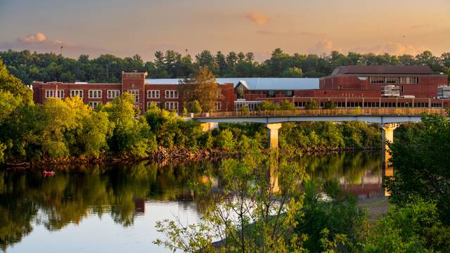 A view of Schofield Hall, a brick building, across the river with the sun setting in vibrant colors