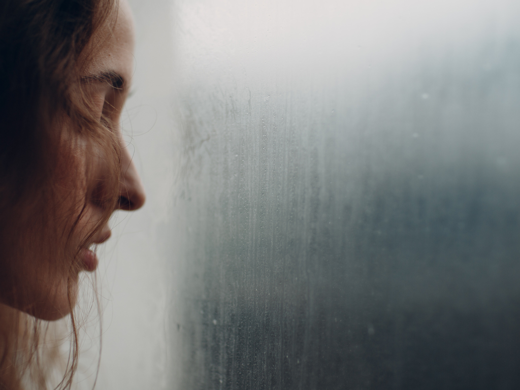 A woman looking troubled outside of a foggy window.