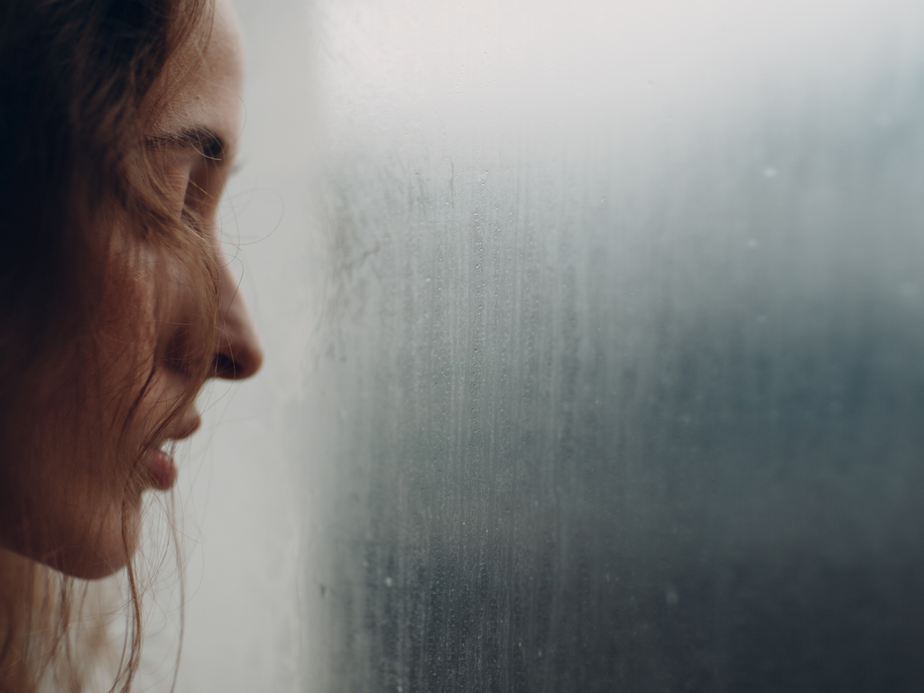 A woman looking troubled outside of a foggy window.