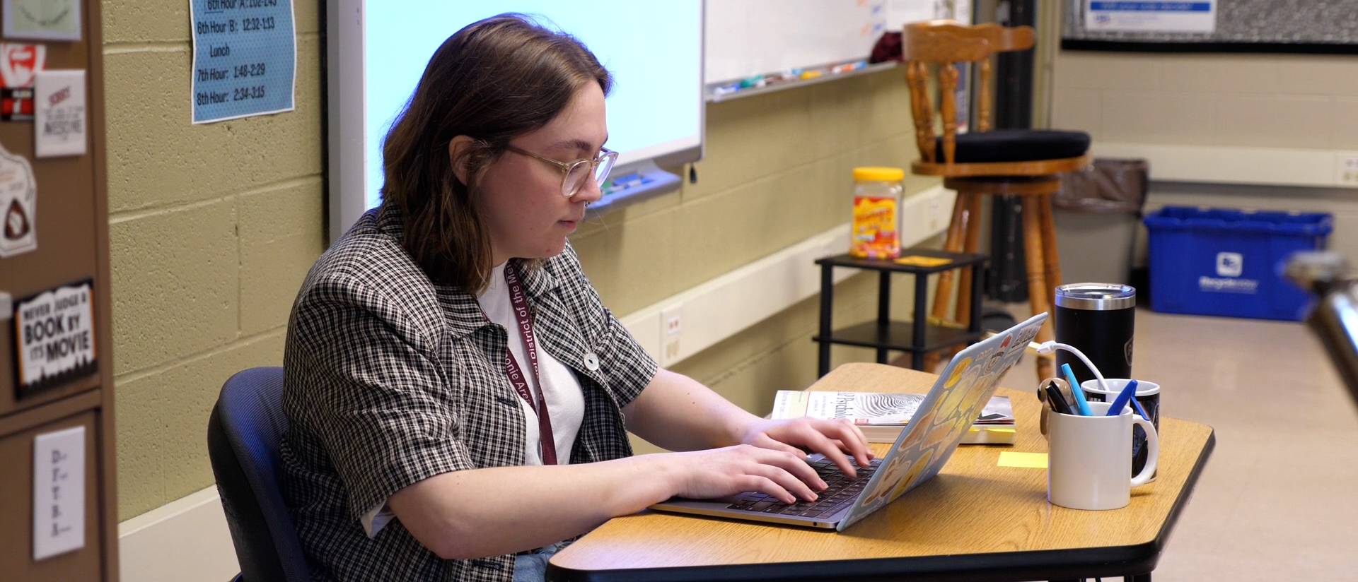 Teacher works at their laptop in a classroom setting
