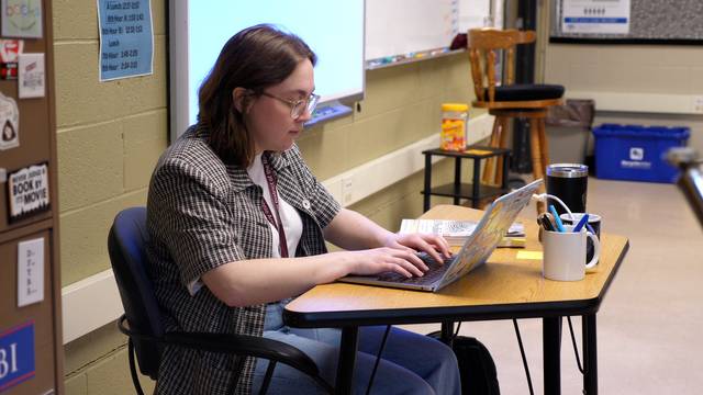 Teacher works at their laptop in a classroom setting