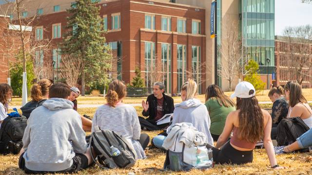 students outdoor for class, sitting on the grass in a circle