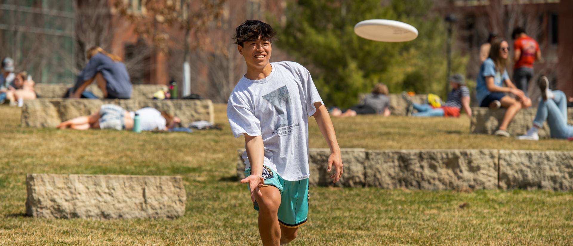 male student throwing a frisbee on campus mall lawn