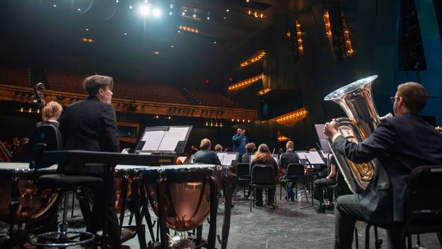 Student dressed formally play instruments in a band concert on stage.