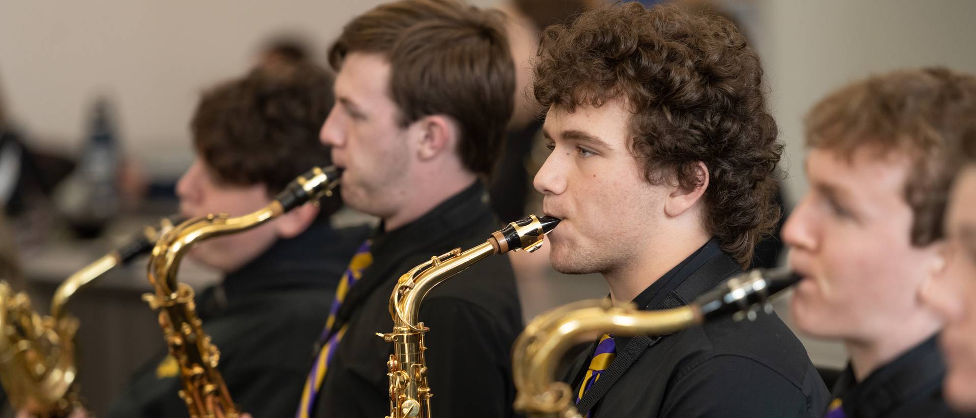 Male students playing saxophone, black shirts with blue and gold ties