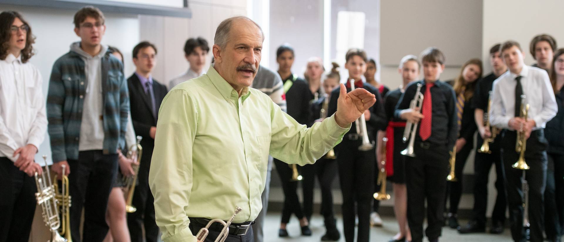 Robert Baca teaching a trumpet master class for 2023 Jazz Fest, standing in front of high school students, yellow shirt