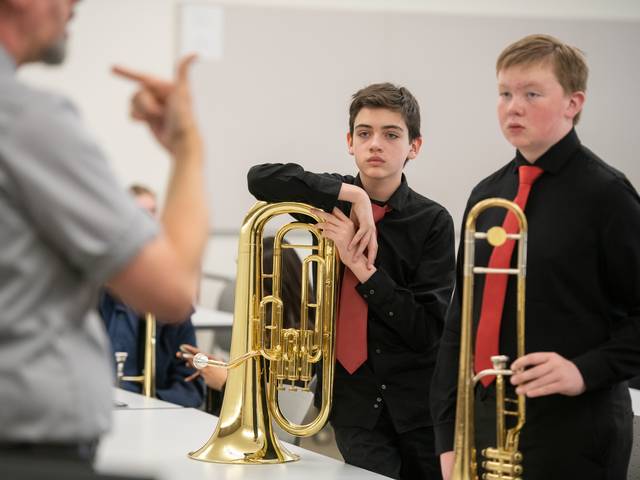 young male trombone students in a mast class listening to speaker