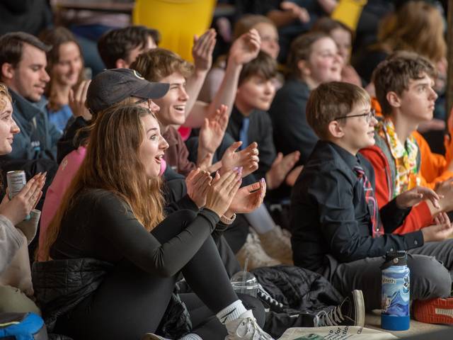 young students cheering in a crowd, seated on the floor