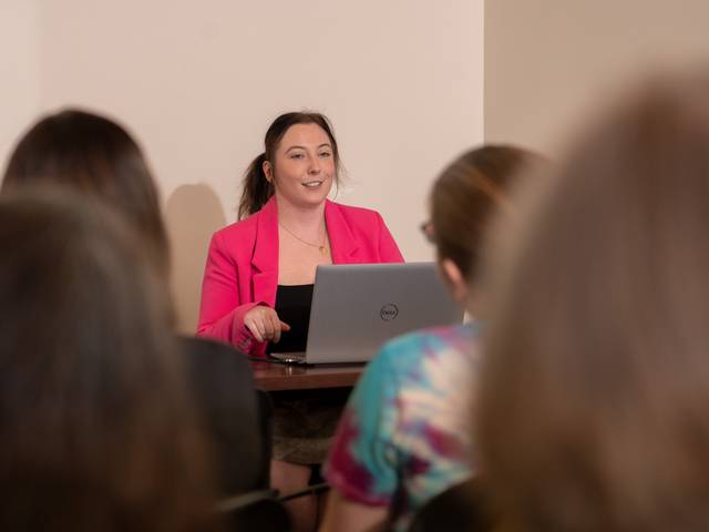 Student presents research to group from behind laptop.