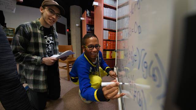 students and faculty doing math on a white board, kneeling