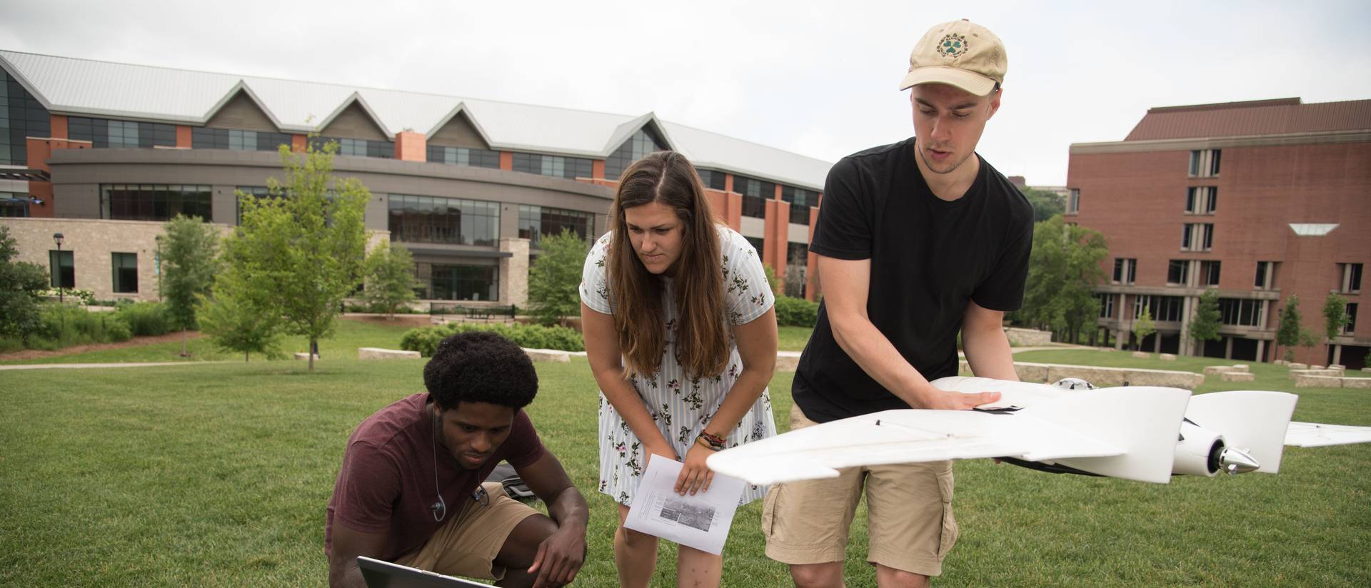 Three students work with a drone on the campus mall.
