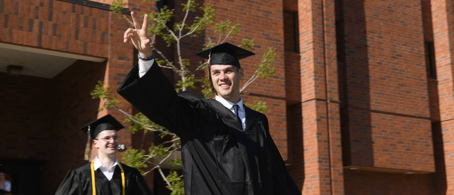 male student in graduate gown giving a peace sign