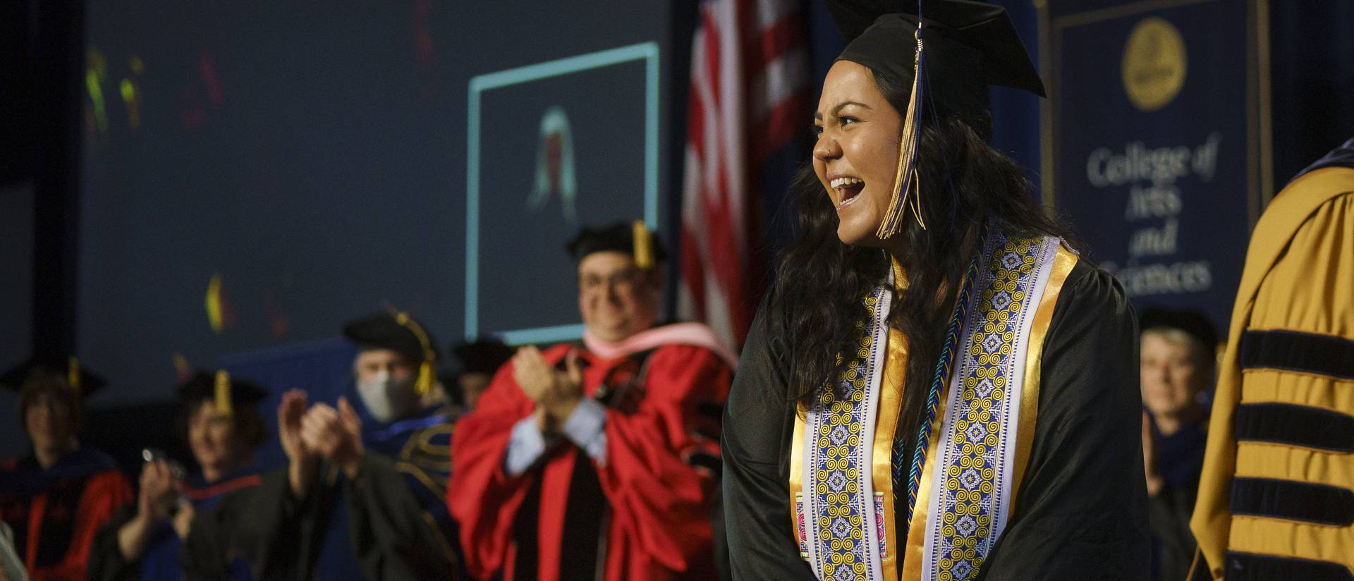 female student on commencement stage smiling at the crowd
