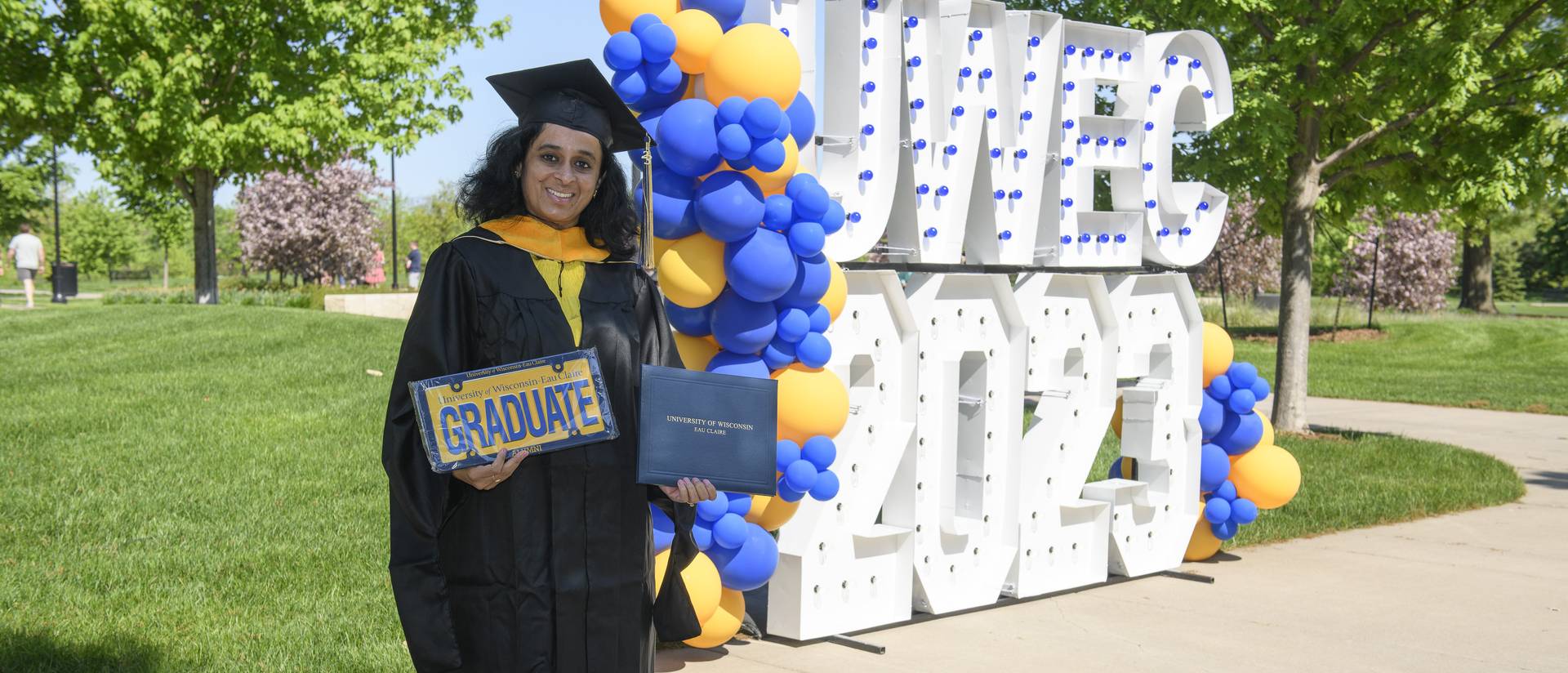 masters student in front of the lighted sign for commencement