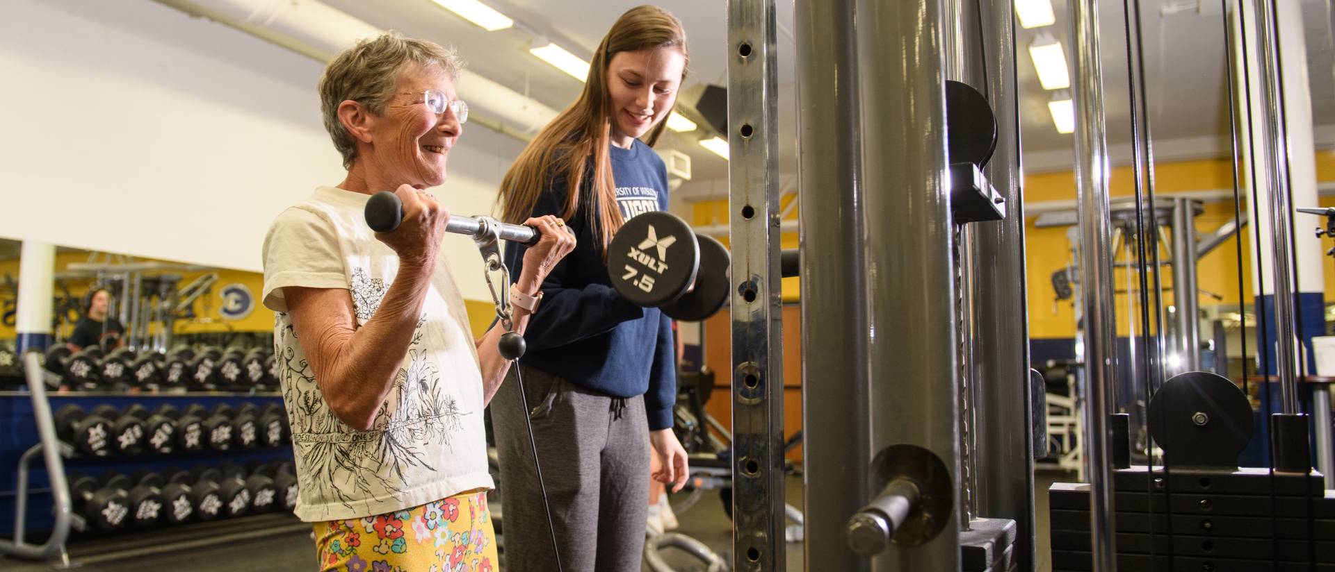 women lifting arms weights in McPhee fitness center with a female student assisting