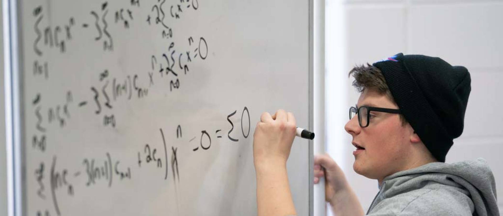 Student in Blugold sweatshirt solves a math problem on a whiteboard.