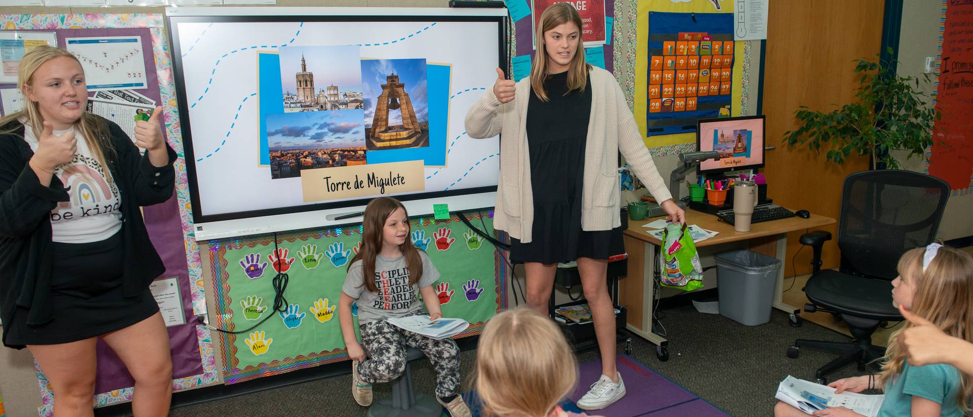 female stuent teachers in front of kids seated on the floor, Spanish words on a white board