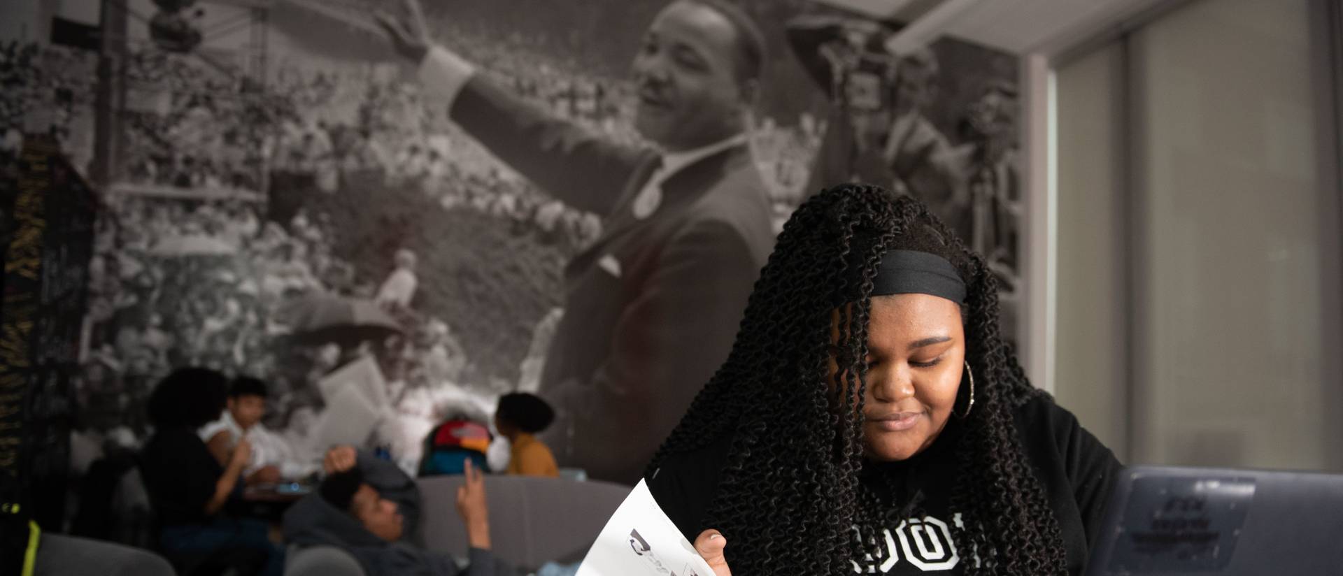 female student studying in the Black cultural center, photo mural of MLK on the wall in the background