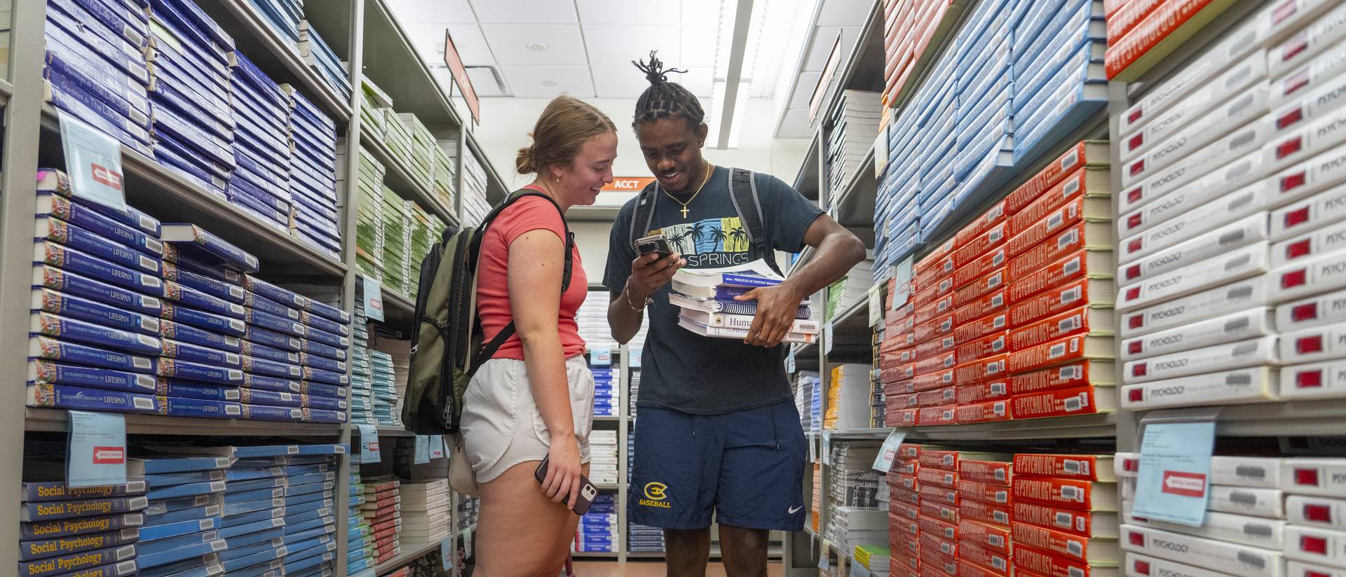 Two students pick out their books between two full bookshelves