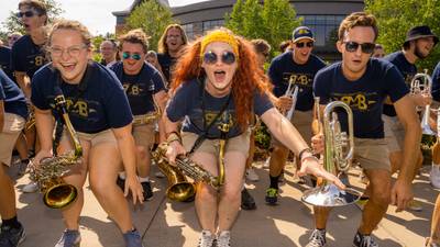 Members of the marching band cheer and pose for a photo with their instruments and matching t-shirts
