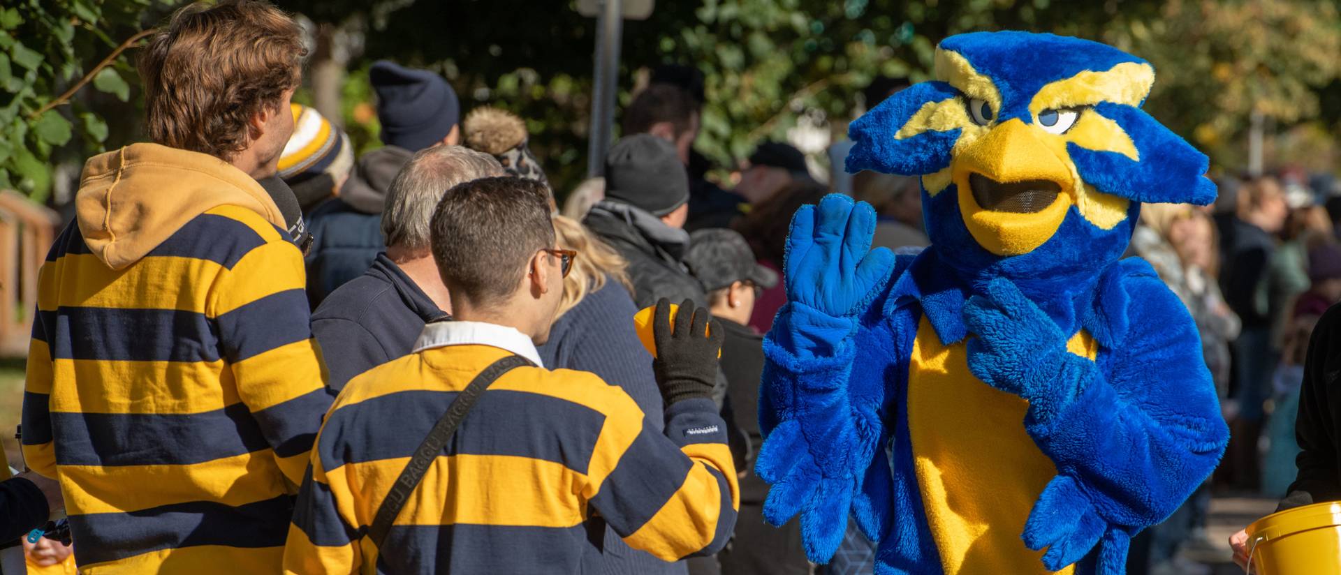 Mascot wearing blue bird suit offers high fives to a crowd attending a parade