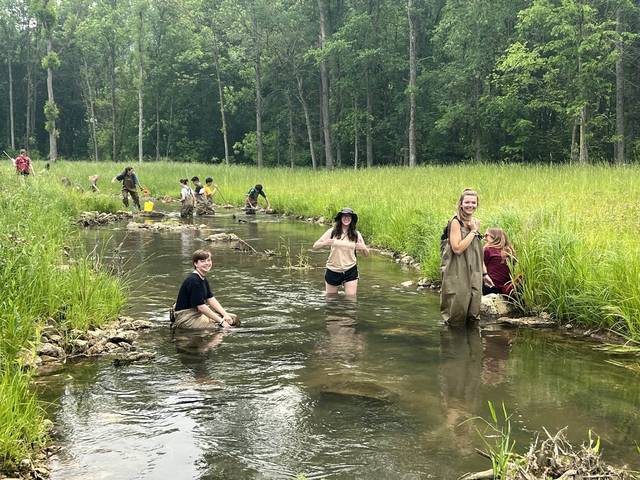 Students smile for a photograph as they wade in a creek conducting an experiment