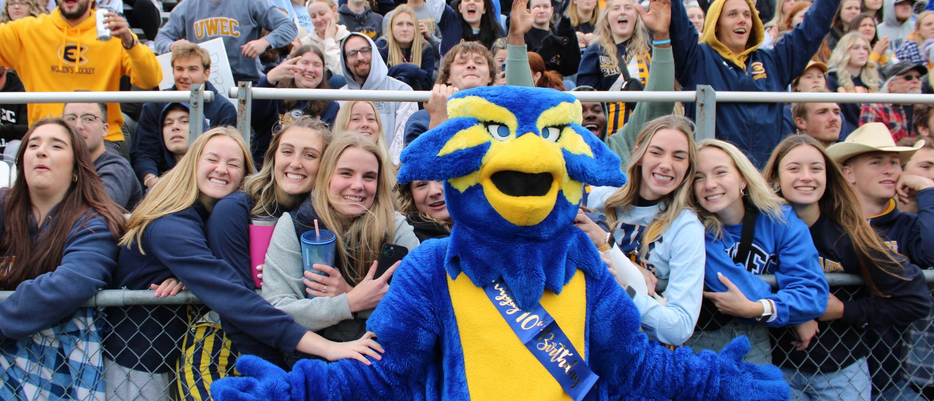 Blu the Blugold in front of a cheering crowd of students at the 2023 Homecoming football game