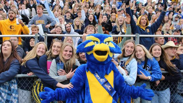 Blu the Blugold in front of a cheering crowd of students at the 2023 Homecoming football game