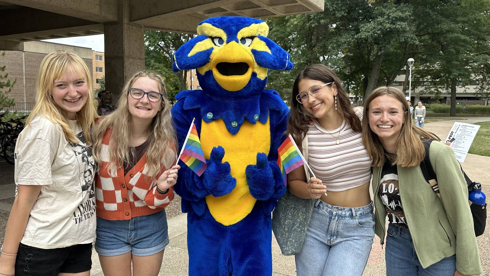 Students standing with Blu, the Blugold Bird Mascot, holding pride flags.