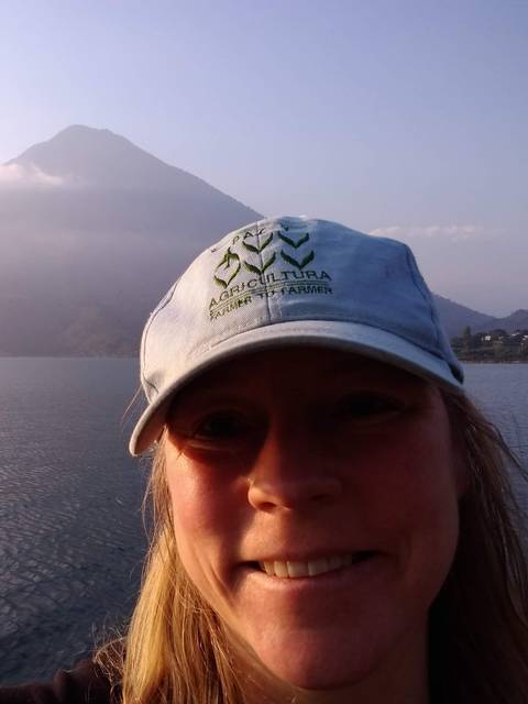 A person smiling in front of water and a mountain