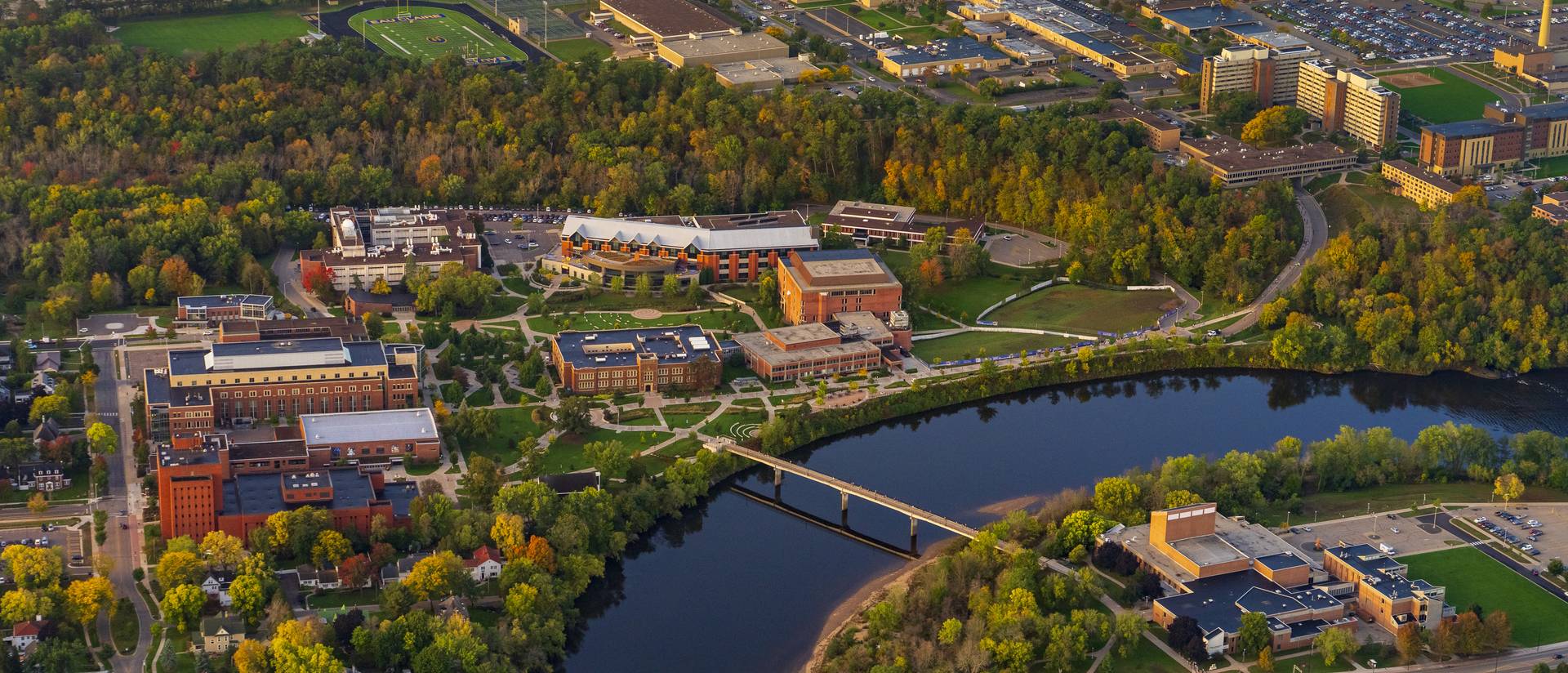 Aerial view of campus showing the river, brick academic buildings and trees turning from green to red and yellow