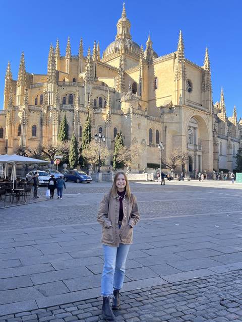 Female student poses in front of an intricately designed stone building while studying abroad