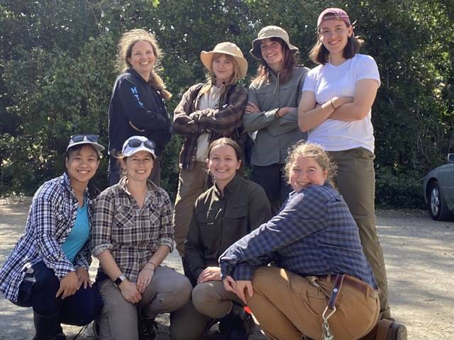 a group of student and faculty researchers outside at a research site, some kneeling some standing; all women pictured