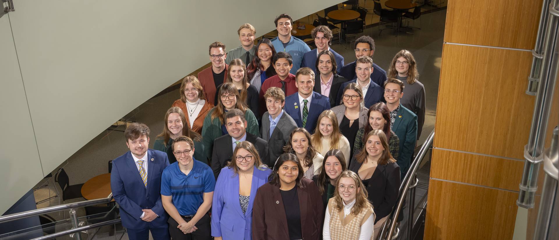 A group of students, standing in stairway, wearing business professional clothing posing for a group photo for the 67th session of Student Senate