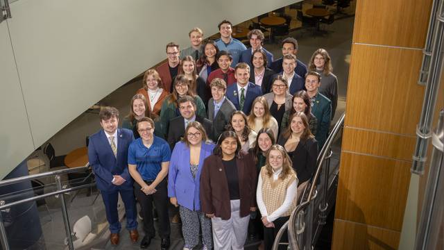 A group of students, standing in stairway, wearing business professional clothing posing for a group photo for the 67th session of Student Senate