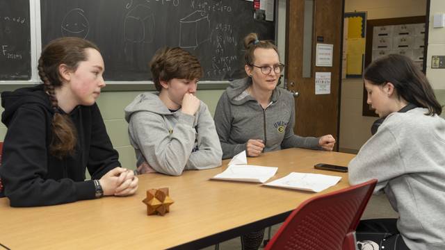 Three students and one faculty at a table; a 3D geometric shape is on the table, they are talking