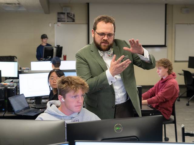 faculty member in suit coat and tie among seated students in a computer science class