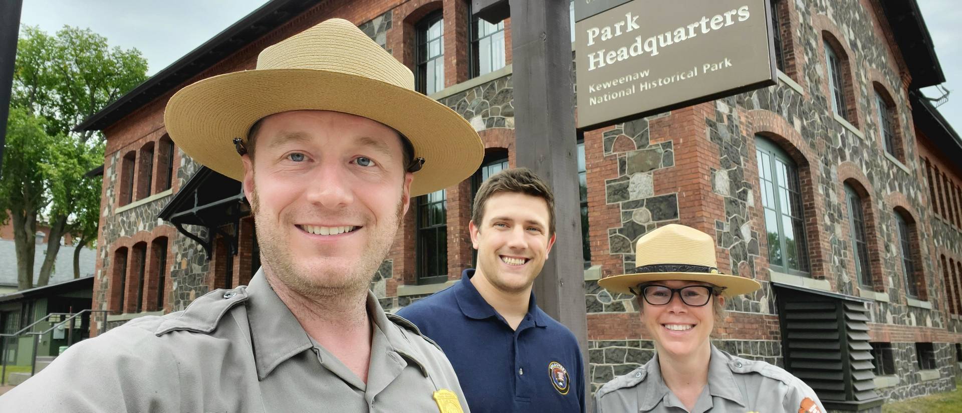 Two National Park Service staff in uniform and one Blugold student outside of a historic building in Michigan