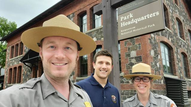 Two National Park Service staff in uniform and one Blugold student outside of a historic building in Michigan