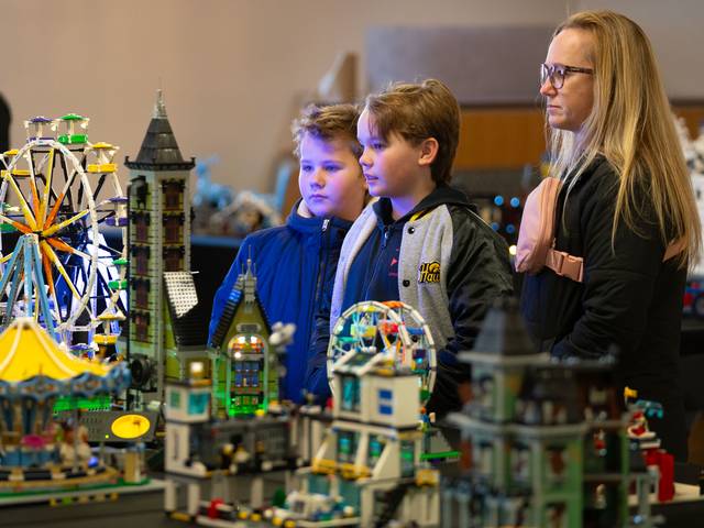 An onlooker and two children look at a Lego display table.