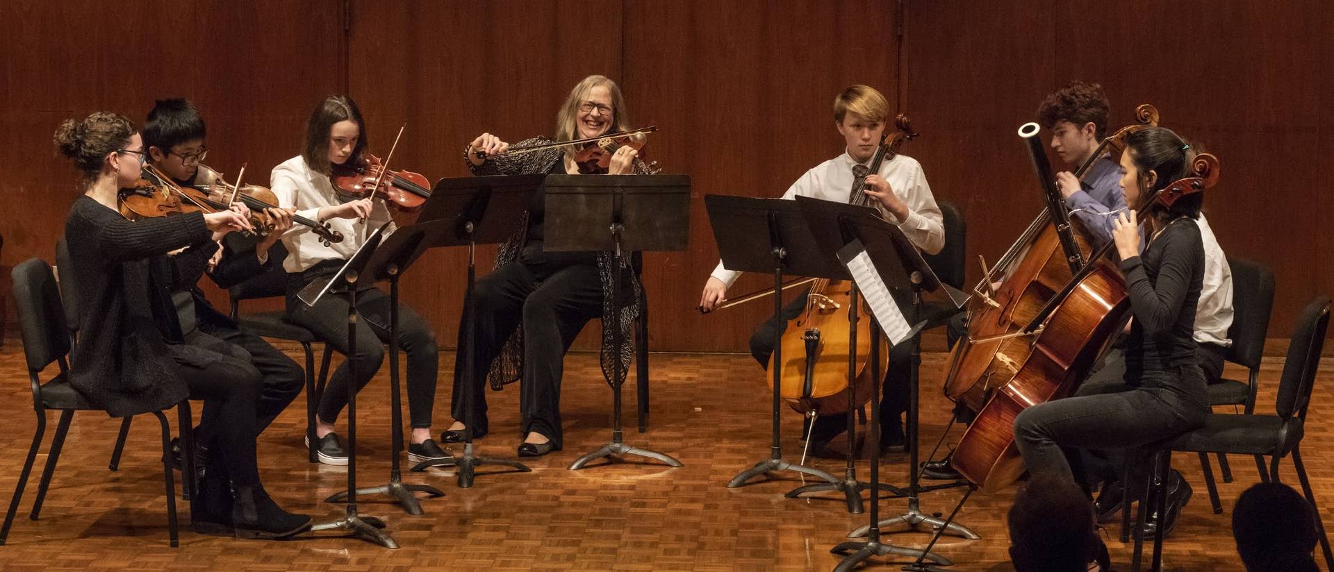 students in a small ensemble playing strings with an instructor