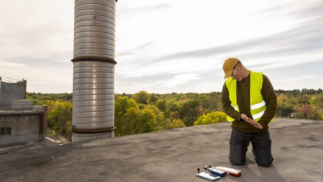 A male student wearing safety gear kneeling on a metal rooftop checking some measurement instruments