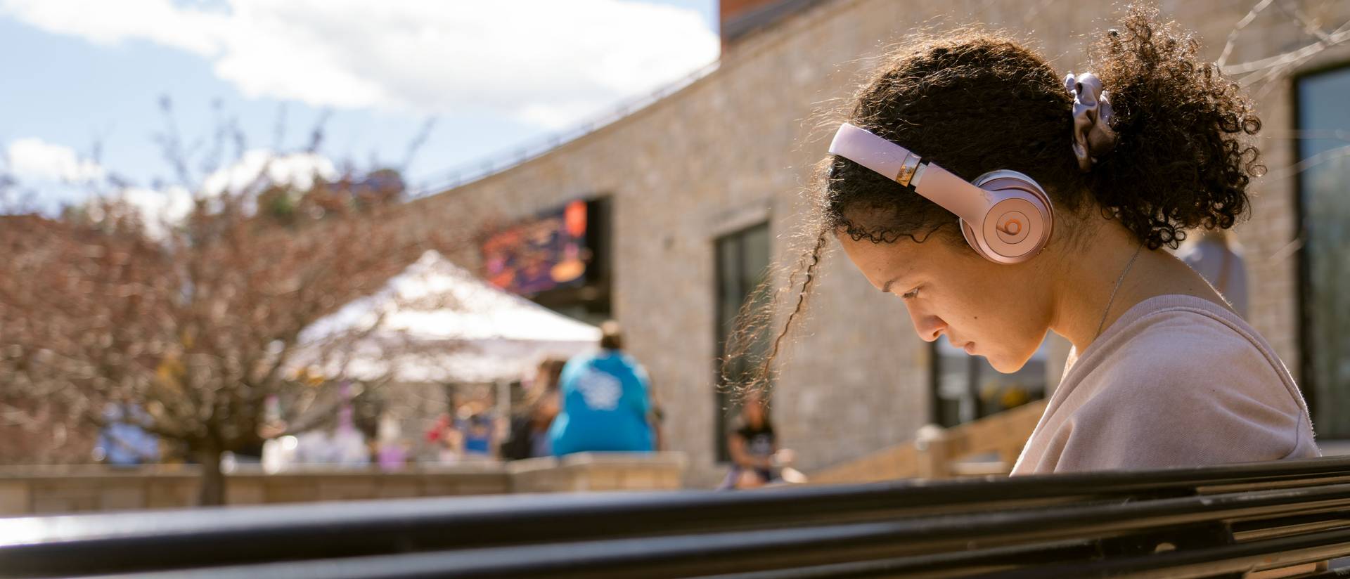 girl on a bench with pink headphones on, curly hair in ponytail