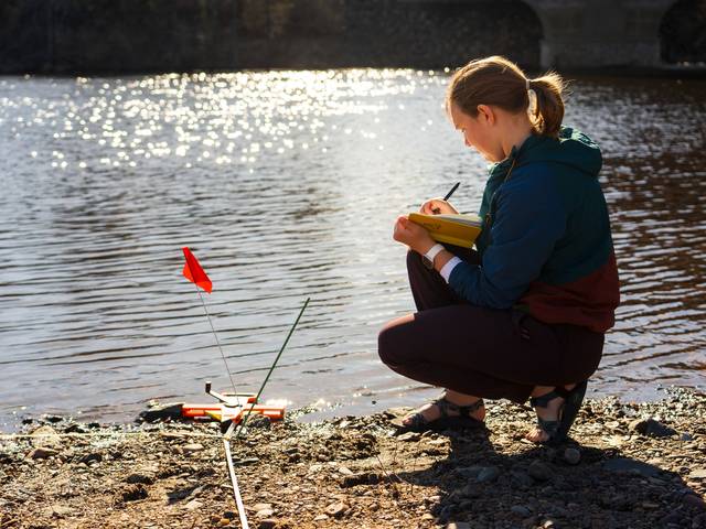 geography survey student by riverbank with measuring tools