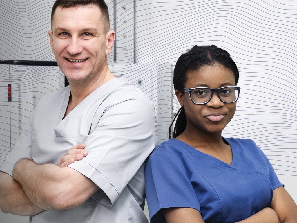 Two medical professionals  standing back to back smiling with their arms crossed.